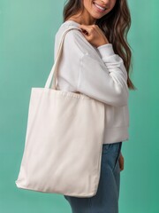 Woman in casual outfit holding a plain canvas tote bag over shoulder against bright teal background. Minimal mockup template showcasing fashion accessory with clean backdrop and copy space.