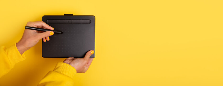 Person holding a digital drawing tablet and stylus against a bright yellow background, emphasizing creative technology and design workspace concepts.