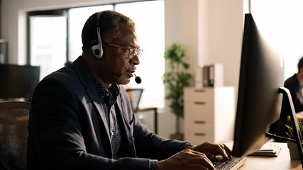 Man typing at computer with headset. Office agent providing customer support in corporate business. Professional focus on typing and communication. Calm workplace for training sales and management.