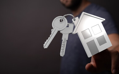 Conceptual image with keys and house shaped keychain in hand, mortgage and real estate ownership. Investment and property concept, housing owner