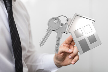Man in a white shirt and tie holding a keychain with a house shape, symbolizing real estate, home ownership, and property investment. The keys
