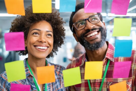 Two smiling coworkers collaborate on colorful sticky notes during a creative team session in the office