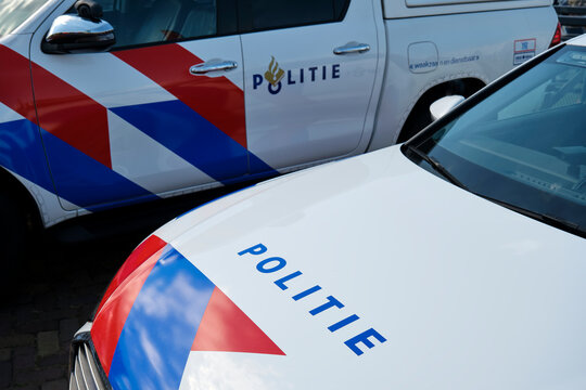 Parked police cars with logo and the word politie in dutch on the side and the hood of t white cars with red and blue stripes in The Netherlands.