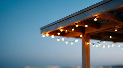 Close-up of warm string lights hanging from wooden pergola against clear evening sky with soft bokeh background