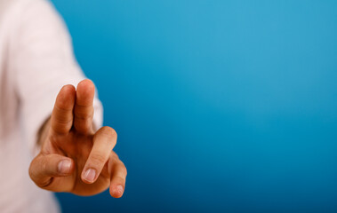 Obraz premium Hand reaching forward with fingers extended, pointing towards empty blue backdrop providing copy space. Concept of touch, technology, selection