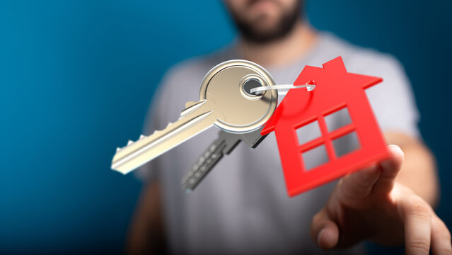 Close up of a man holding a key and red house keychain, symbolizing home ownership and real estate. Perfect for mortgage, investment themes. - Powered by Adobe