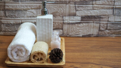 Beautiful spa composition with towels and spa set accessories on wooden tray placed on wooden floor, background is light colored brick.