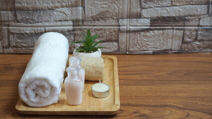 Beautiful spa composition with towels and spa set accessories on wooden tray placed on wooden floor, background is light colored brick.