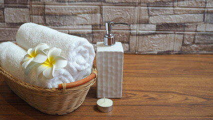 A tranquil spa setting with rolled up white towels in a wooden basket, frangipani flowers, soap...