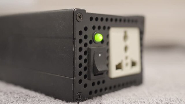 A hand operates the plastic switch on the metal power converter. The device turns on with a distinct click, a green indicator light glows, and the cooling fan starts with a noticeable whirring noise.