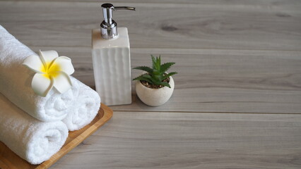 A serene spa setup featuring rolled white towels, a plumeria flower, a soap dispenser, and a small succulent plant on a wooden tray, creating a clean and relaxing wellness atmosphere.