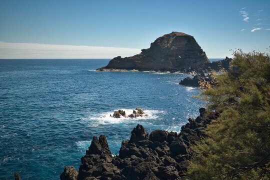 A rocky shoreline with a large rock in the middle of the ocean
