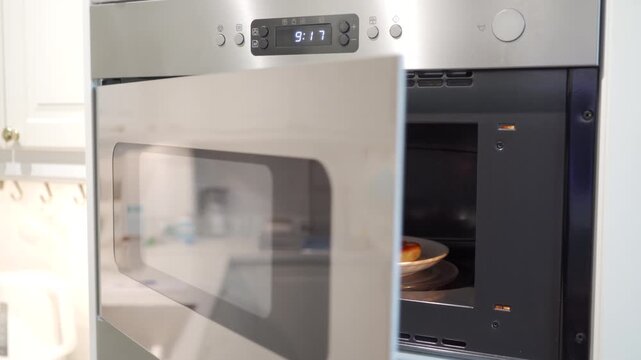 After heating, the stainless steel microwave remains open with a plate of food inside. The appliance emits a low humming noise as it cools down.