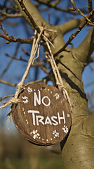 Environmental message sign “No Trash” displayed on a wooden board attached to a tree in a natural forest setting. Promotes sustainability and conservation awareness