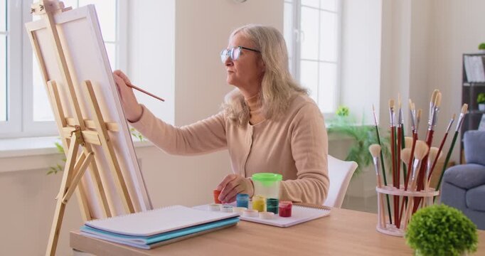 Painting hobby, senior woman creating picture, female painter working at easel using paintbrush on canvas, creative activity studio, beginner spending retirement in workshop, learning how to paint
