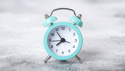 A close-up shot of a small, light blue alarm clock with a white face on a gray surface with a shallow depth of field.