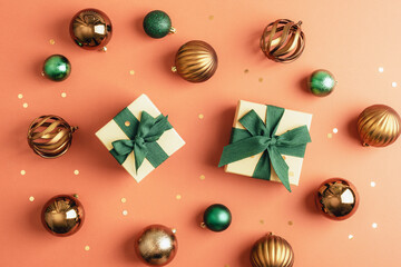 Christmas gifts with green ribbons and bronze ornaments on orange background. Top view, flat lay