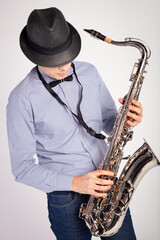 Fototapeta premium Portrait of stylish man in hat playing saxophone, performing isolated over white background. Jazz performer