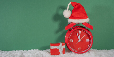 Merry Christmas, year 2025 or saint nicholas day, celebration holiday greeting card - countdown, santa hat on red retro alarm clock and gift box in snow, isolated on green background
