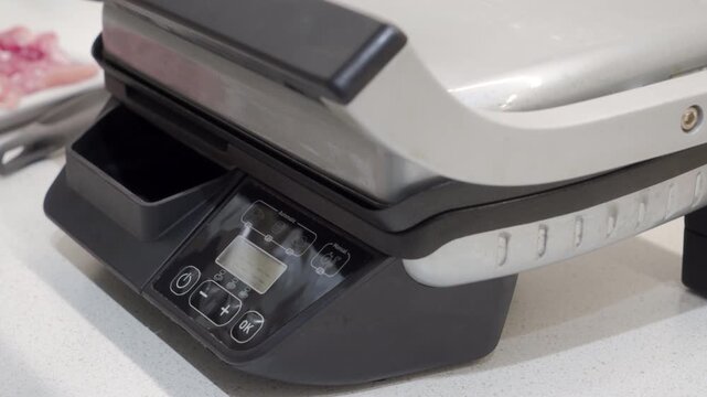 The metal and plastic electric grill is preheating on the countertop. The internal heating elements generate a clear, random crackling and popping sound.