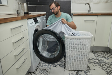 Man doing laundry at home in modern kitchen. Person loading washing machine and pouring detergent. Concept of household chores, domestic life, and home cleaning routine