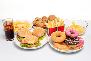 Hamburger, fried chicken, donuts and french fries on plate on white table, unhealthy fast food, studio shot, close up