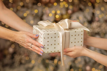 Hands of parent giving Christmas gift to child on Christmas tree background
