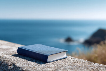 Blue book rests on a stone wall with the sea blurring in the background, suggesting travel, reading, vacation, or escape. Ideal for educational, inspirational, or travel content.