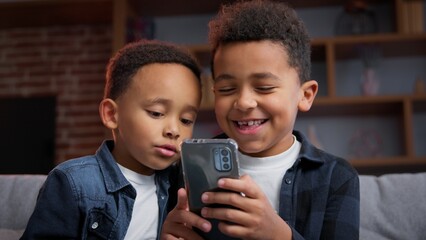 Two African American little boys looking phone carefree cheerful brothers with mobile apps...