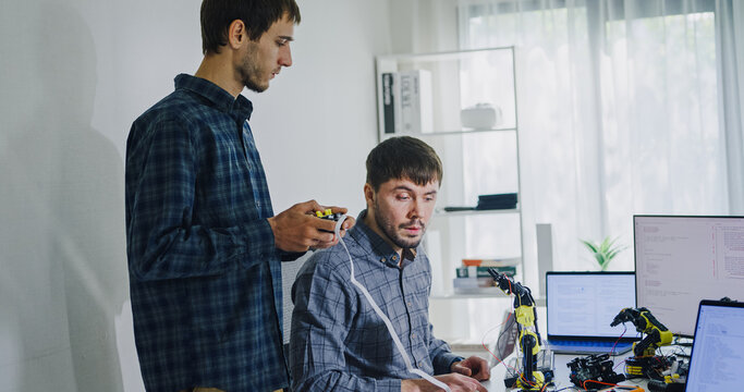 Team adult male engineer collaborate on robotic hand project using AI code solutions machine learning at tech workspace. Artificial intelligence interface, collaboration support prototype development.