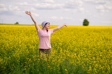 Woman in bucket hat raising arms up, enjoying a warm summer day in a blooming yellow rapeseed field