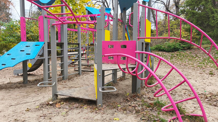 A vibrant playground with slides and climbing walls, set in a park surrounded by autumn trees, provides a lively and joyful space for children to play outdoors.