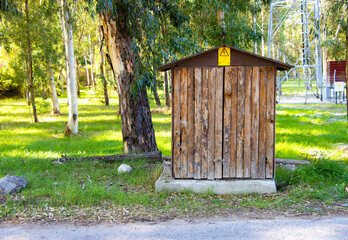 Small wooden utility shed with electrical hazard warning sign—captured in grassy outdoor setting...