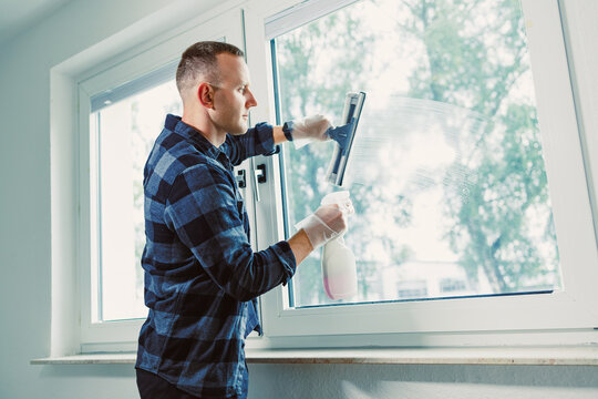 Man carefully cleaning a window in a bright room during a sunny day, showcasing attention to detail and the importance of a clean home environment