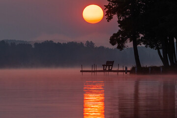 Tranquil sunrise over misty lake with dock and trees