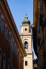 Beautiful view of an old brick church tower framed by colorful Italian buildings under a clear bright blue sky.