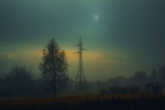 Lonely power line tower in foggy autumn field
