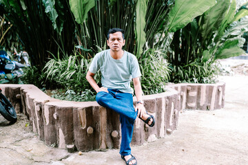 Asian Man Posing on Decorative Wall in Green Garden
