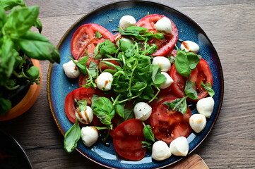 Top view of a fresh Caprese salad with baby mozzarella, ripe tomatoes, and herbs. The colorful and vibrant presentation highlights the freshness of the ingredients and the simplicity 