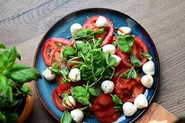 Top view of a fresh Caprese salad with baby mozzarella, ripe tomatoes, and herbs. The colorful and vibrant presentation highlights the freshness of the ingredients and the simplicity 