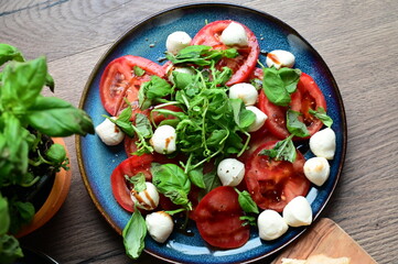 Top view of a fresh Caprese salad with baby mozzarella, ripe tomatoes, and herbs. The colorful and vibrant presentation highlights the freshness of the ingredients and the simplicity 