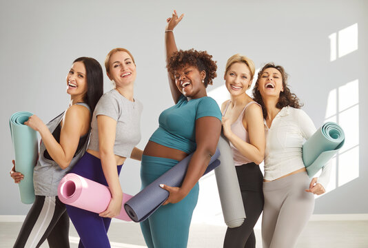 Happy group of young sporty girls, afro american woman and caucasian fit people with yoga mats standing, female companions in gym after fitness, instructor and club team after practicing sport lesson
