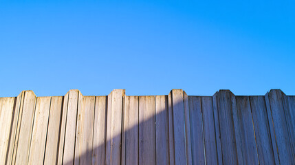 perfectly aligned and symmetrical tall wooden fence with chamfered tops with a blue sky. 