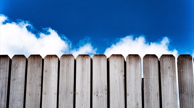 perfectly aligned and symmetrical tall wooden fence with chamfered tops with a blue sky. 