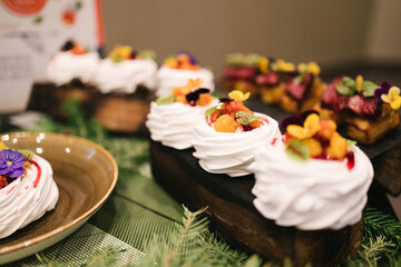 Elegant Pavlova desserts with meringue bases, topped with fresh berries, edible flowers, and creamy...
