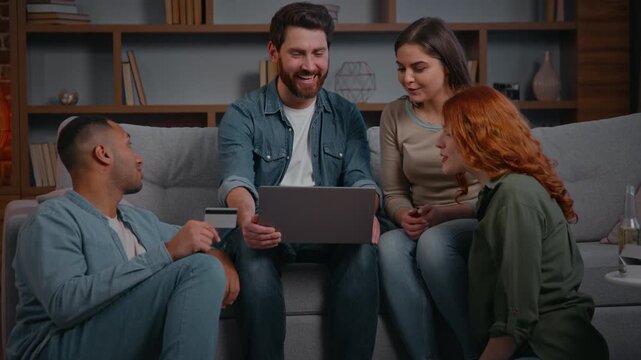 Excited multiracial four friends shopping online together ordering food delivery for home party on couch diverse men women using credit card internet payment on laptop celebrate success money cashback