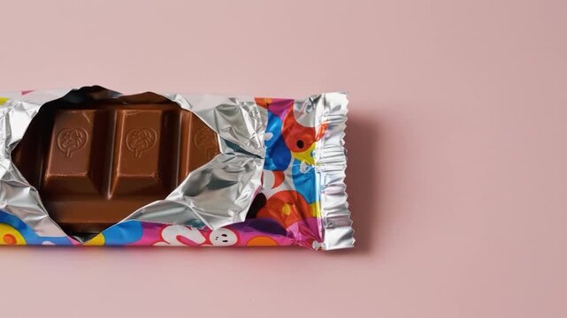 Milk chocolate bar in colorful wrapper on pink background