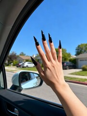 Stylish hand with long black stiletto nails reaching out car window on sunny day, capturing freedom and modern flair
