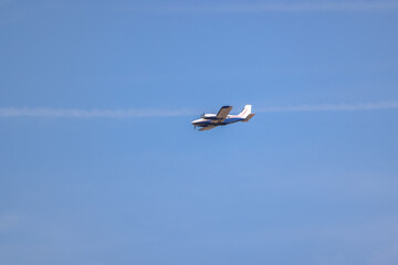 A small twin-engine airplane flies high against a clear blue sky, leaving faint vapor trails behind. The simplicity and freedom of air travel, perfect for aviation, transportation, or travel concepts.