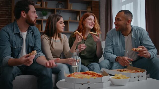 Four multiracial group friends at home party tasting pizza team of diversity people talking friendly drinking alcoholic beverages enjoying delivery food men women at couch sofa event fun hanging out